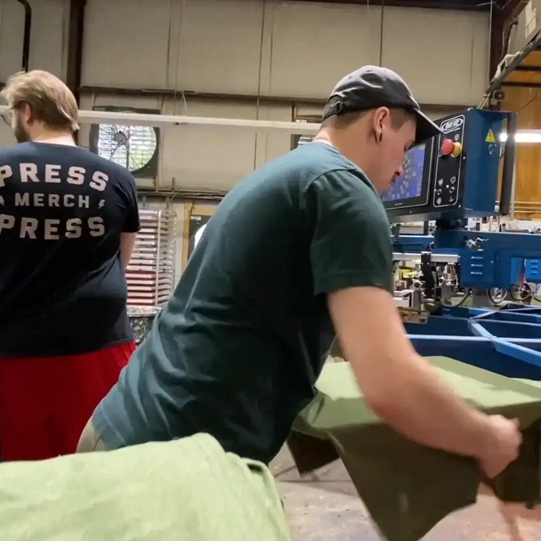 Two of our production team members feeding and pulling shirts from the automatic press